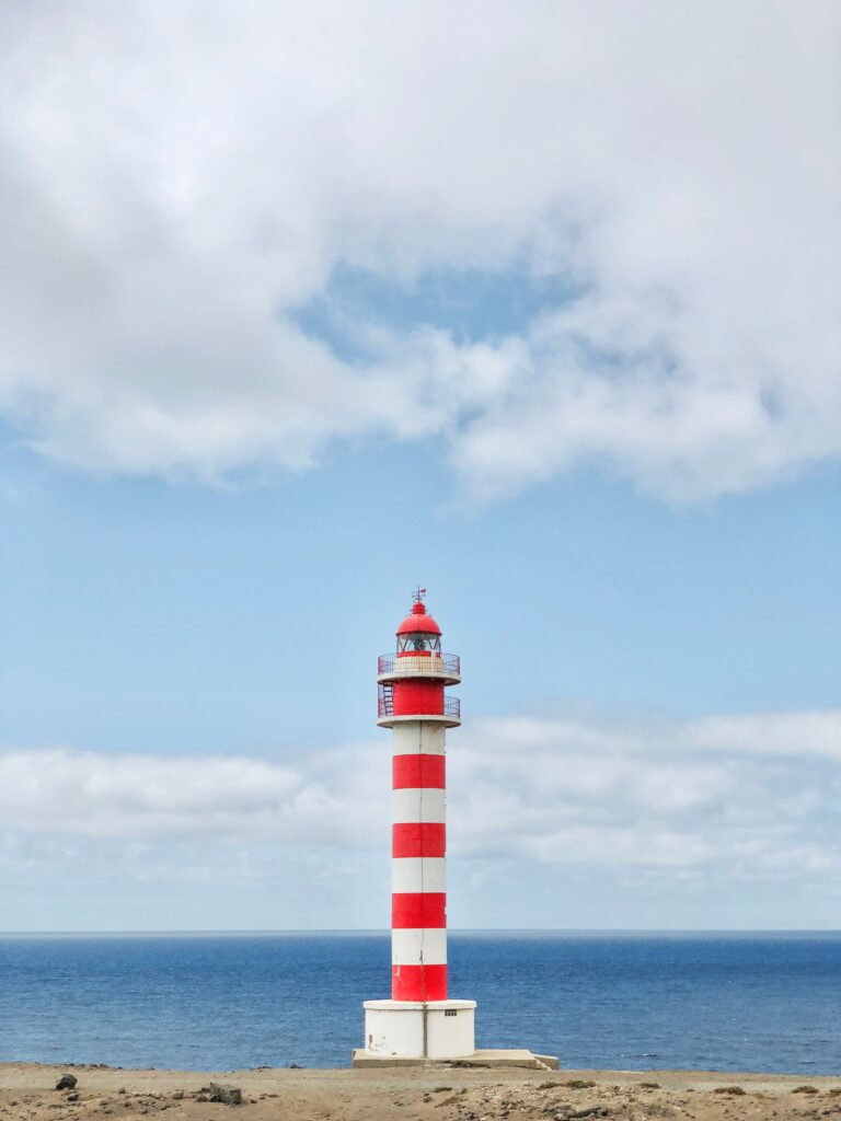 Red and white lighthouse against blue sky